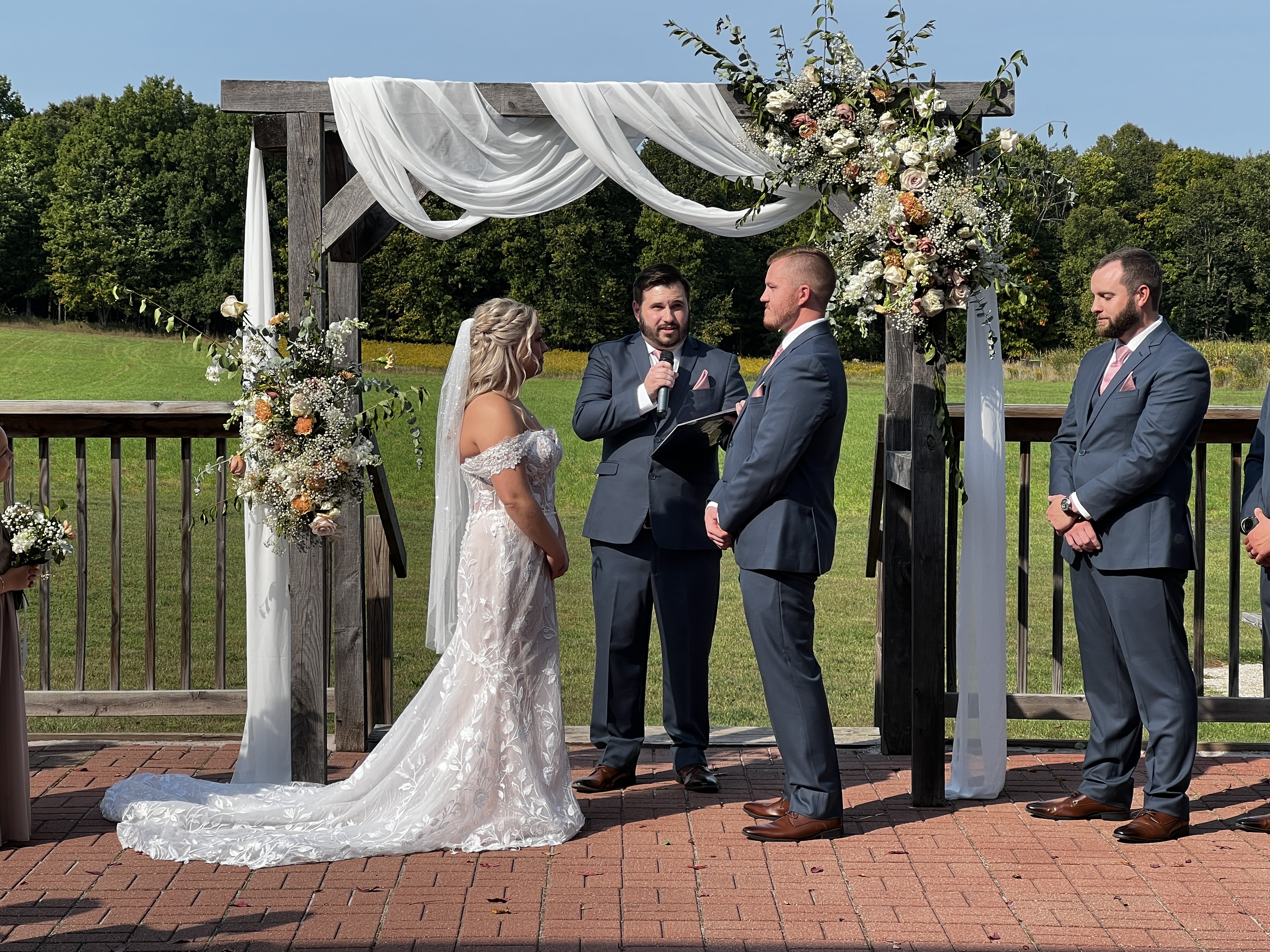 A bride and groom share a joyful first kiss beneath a rustic outdoor arbor